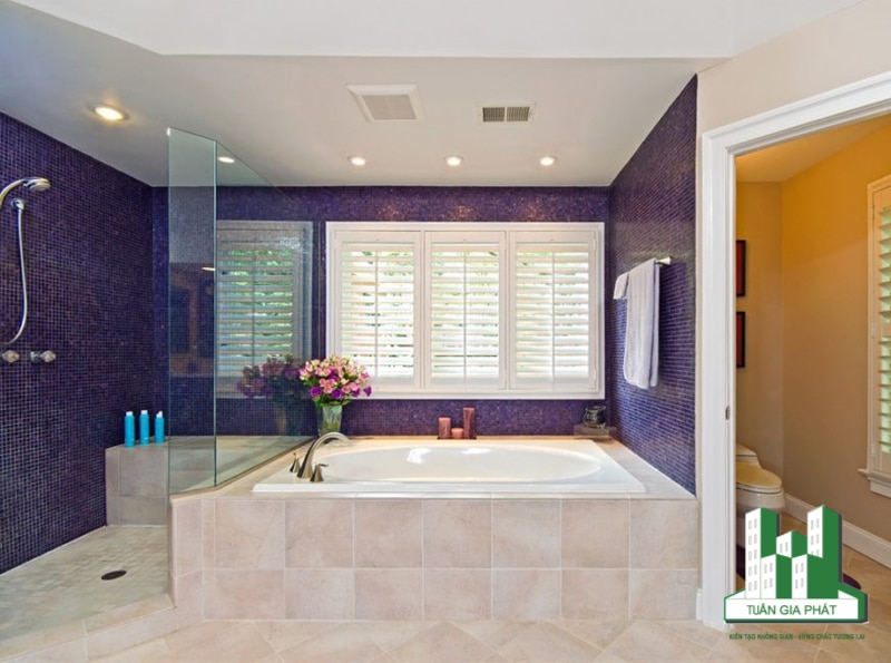 Bức tường phía bồn tắm và bàn khu vực bồn rửa nổi bật với màu tím đậm tạo điểm nhấn cho căn phòng. Phần nhà tắm phía bên trong ốp gạch đen cũng làm tăng nét hiện đại.