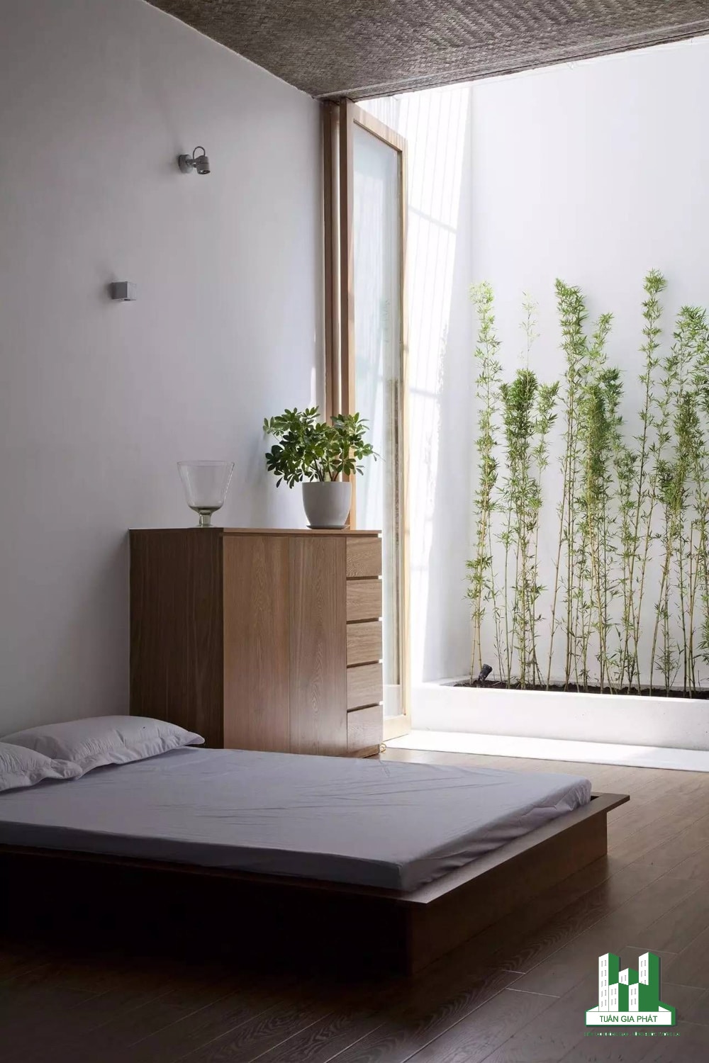 Phòng ngủ Zen tối giản với đồ nội thất bằng gỗ, bộ khăn trải giường màu trắng. Phòng có một cửa kính dạng gấp kết nối thông với không gian ngoài trời.