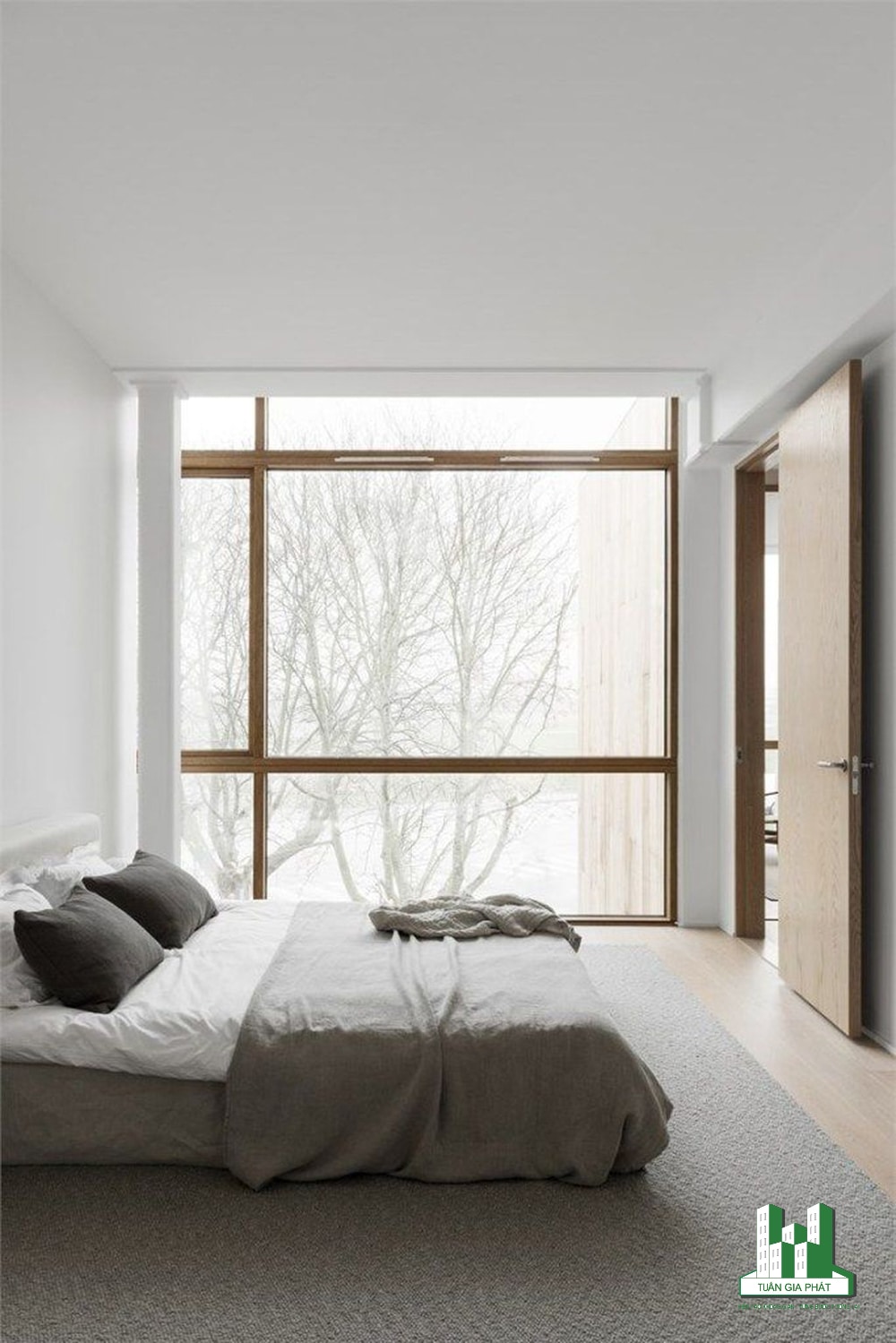 Phòng ngủ Zen trung tính với giường ngay trên sàn và tường lắp kính để thưởng ngoạn quang cảnh bên ngoài cùng bộ khăn trải giường cũng cùng tone màu trung tính.
