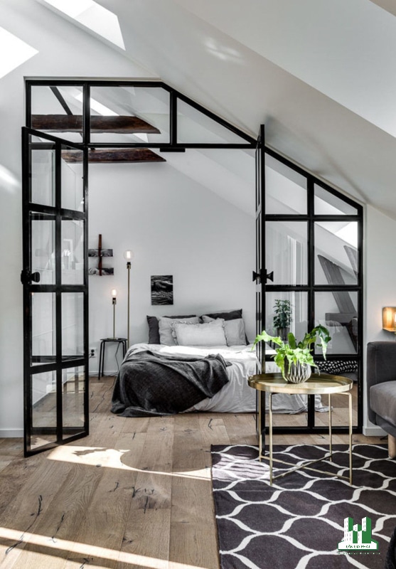 Phòng ngủ vách ngăn bằng kính phong cách Bắc Âu với giường ngủ, tủ đầu giường, cửa sổ trần, đèn bàn và bức tường kính để kết nối nó với phần còn lại của không gian.
